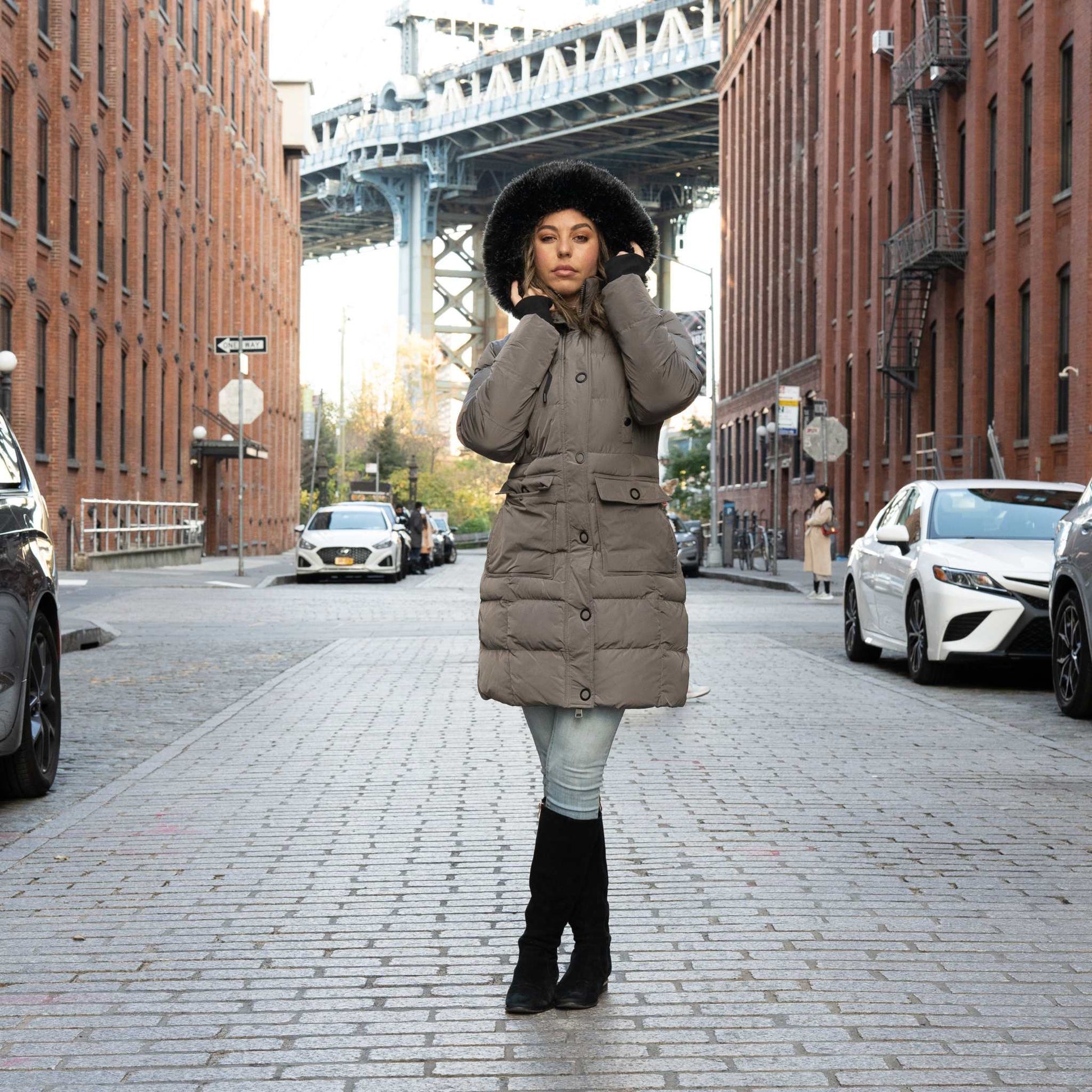 Woman wearing ELORA Down Vegan Heavy Women's Winter Coat with faux fur hood, standing in urban street setting.